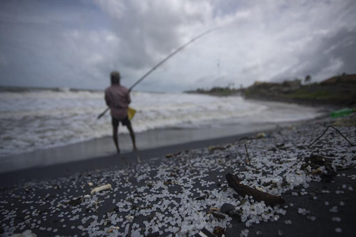 Sri Lankan man fishes on a polluted beach filled with plastic pellets