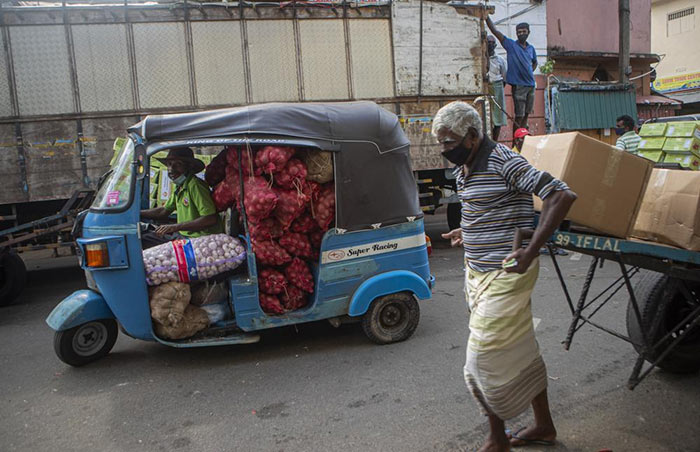 A Sri Lankan man transports a load of imported onions and garlic in an autorickshaw