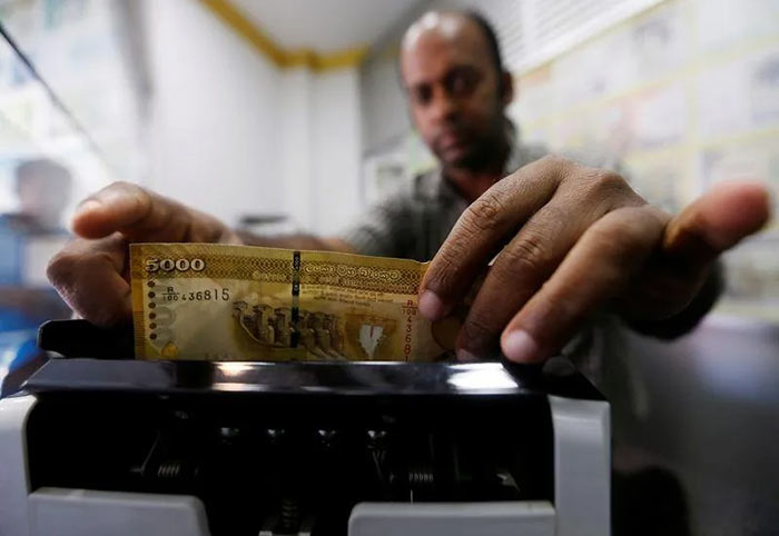 A man counts Sri Lankan rupees in a note counting machine at a money exchange counter in Colombo