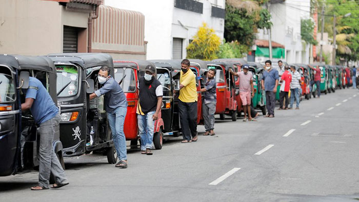 Drivers push their three wheelers to buy petrol at a fuel station in Colombo, Sri Lanka