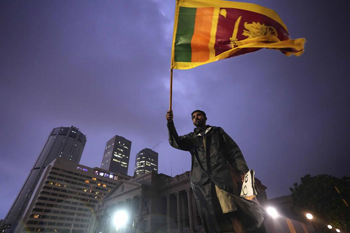 A man waves a Sri Lankan national flag as he stands on a barricade blocking the entrance to president's office during a protest in Colombo, Sri Lanka
