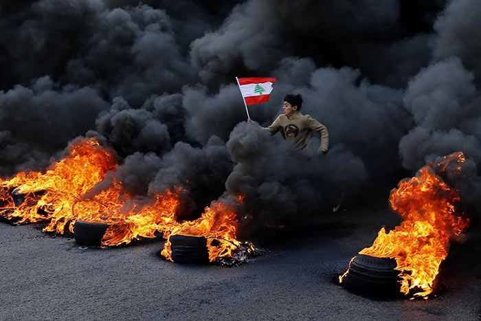 An anti-government demonstrator holds a national flag and runs across tires that were set on fire in the town of Jal el-Dib, north of Beirut, Lebanon