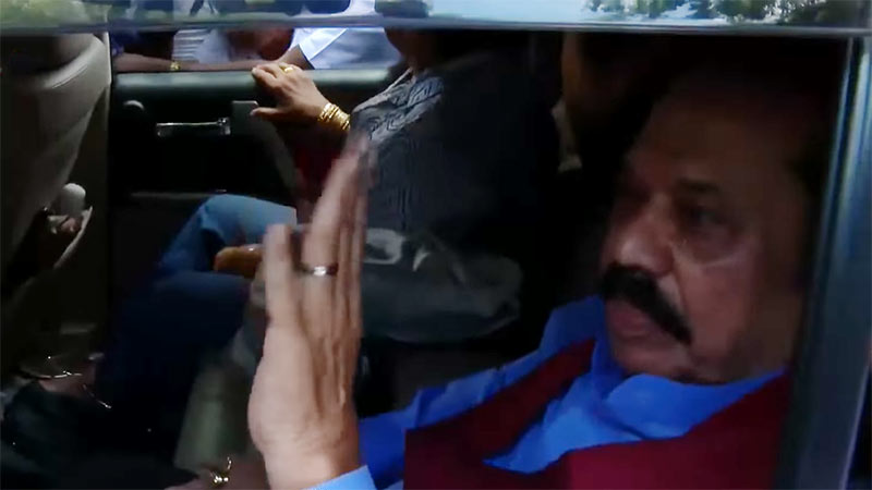 Former Sri Lanka President Mahinda Rajapaksa and his wife seated in the back of a vehicle, waving to the crowd