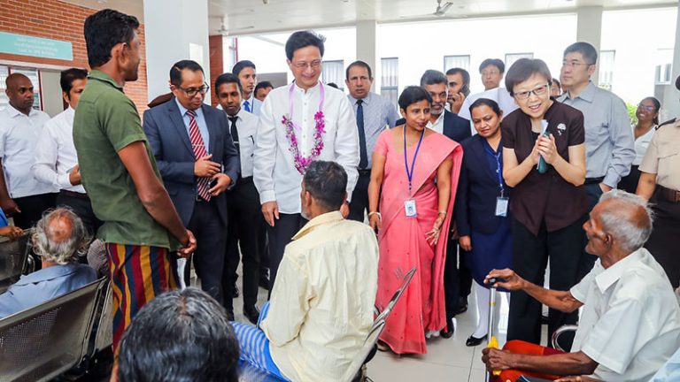 Chinese Ambassador to Sri Lanka, Qi Zhenhong speaking with patients seated on public chairs, accompanied by Sri Lanka Parliament Speaker Jagath Wickramaratne and officials at Polonnaruwa event