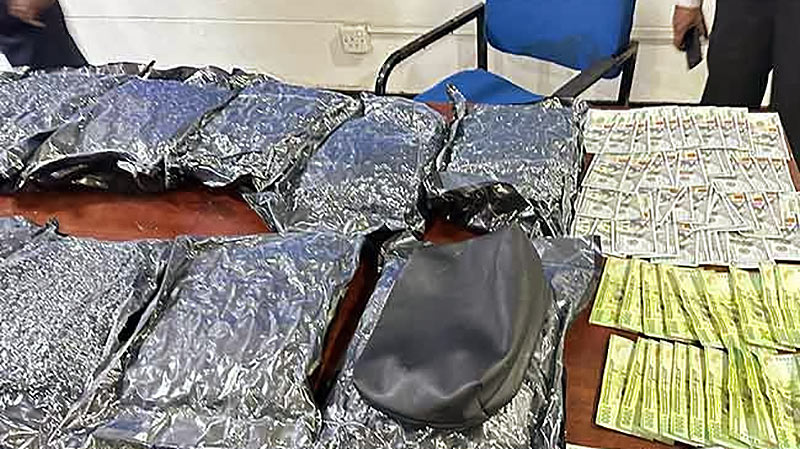 Seized cannabis, cash, and luggage displayed on a table following a drug trafficker's arrest