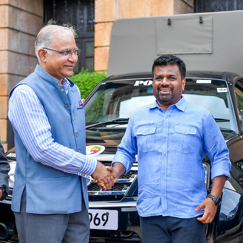 Indian High Commissioner to Sri Lanka Santosh Jha shakes hands with Sri Lankan President Anura Kumara Dissanayake in front of a donated vehicle