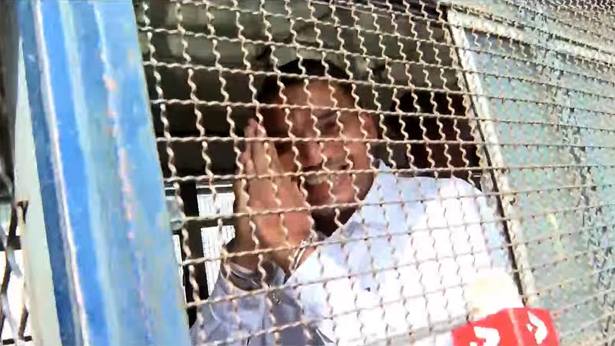 Namal Rajapaksa smiling at cameras from behind the steel mesh of a prison bus outside the Colombo Fort Magistrate’s Court