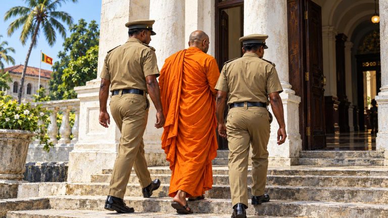A Buddhist monk in saffron robes being escorted into a Sri Lankan court by two prison officers